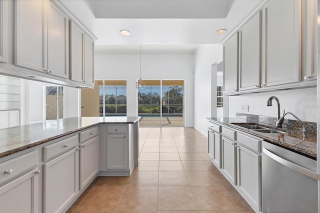 kitchen featuring gray cabinetry, sink, stainless steel dishwasher, dark stone countertops, and light tile patterned floors