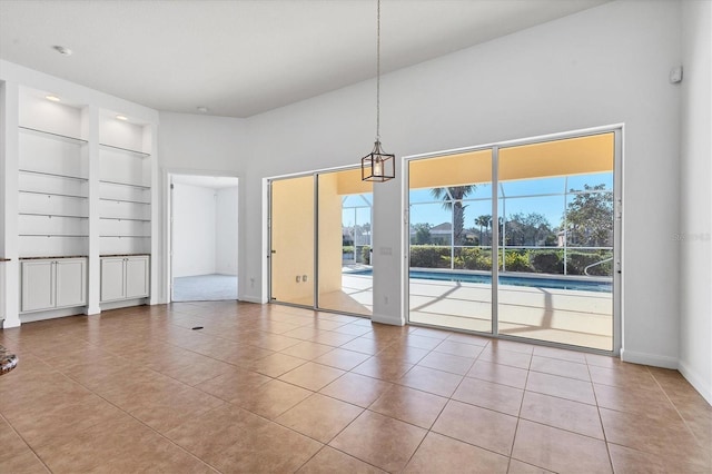 tiled empty room featuring built in shelves and a towering ceiling