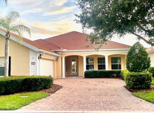 mediterranean / spanish house with a garage, a tile roof, decorative driveway, and stucco siding