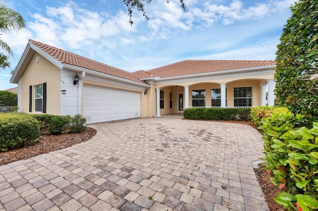 mediterranean / spanish home with decorative driveway, a tiled roof, an attached garage, and stucco siding