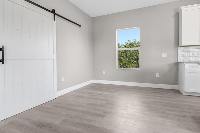 unfurnished bedroom with a barn door and light hardwood / wood-style floors