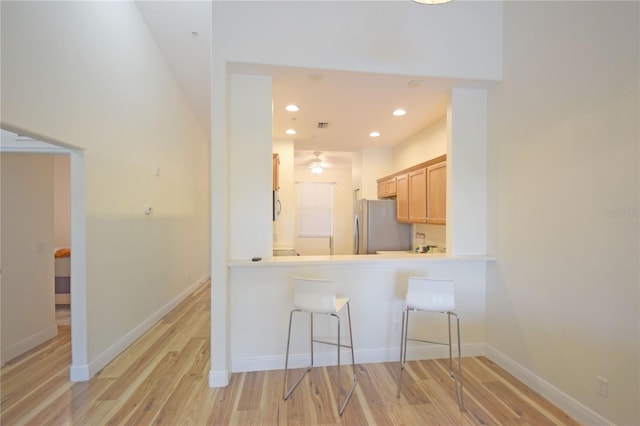 kitchen featuring ceiling fan, light brown cabinets, stainless steel fridge, a kitchen bar, and light wood-type flooring