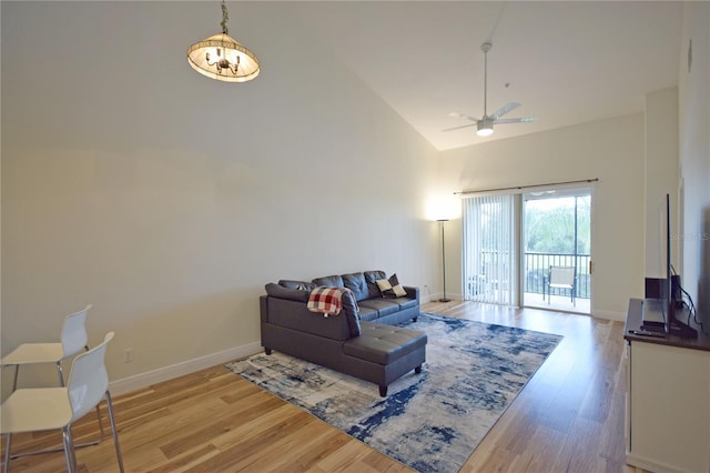 living room featuring light wood-type flooring, ceiling fan with notable chandelier, and high vaulted ceiling