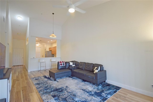 living room featuring light hardwood / wood-style flooring, high vaulted ceiling, and ceiling fan