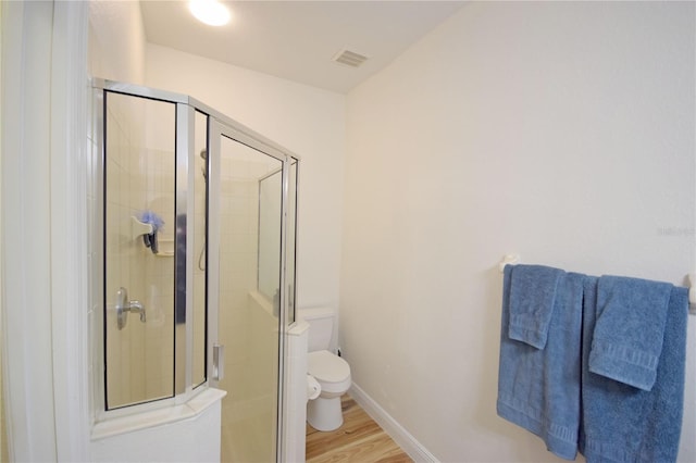 bathroom with hardwood / wood-style floors, toilet, and a shower with shower door