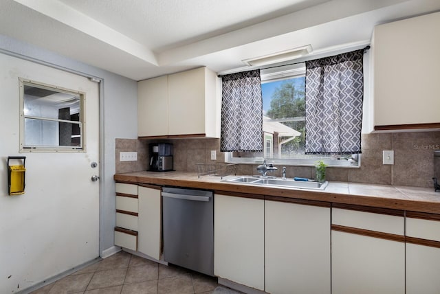 kitchen with backsplash, sink, light tile patterned floors, dishwasher, and white cabinetry