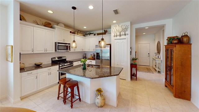 kitchen featuring an island with sink, stainless steel appliances, pendant lighting, dark stone countertops, and white cabinets