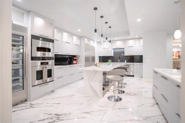 kitchen featuring a large island, hanging light fixtures, a raised ceiling, decorative backsplash, and white cabinets