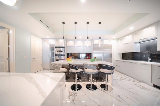 kitchen featuring white cabinetry, a raised ceiling, pendant lighting, a breakfast bar area, and high end fridge