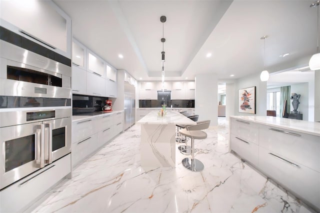 kitchen featuring pendant lighting, a raised ceiling, a kitchen island, white cabinetry, and a breakfast bar area