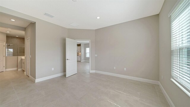 unfurnished bedroom with light tile patterned flooring, multiple windows, and connected bathroom