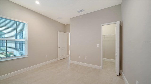 unfurnished bedroom with a closet, multiple windows, a spacious closet, and light tile patterned floors