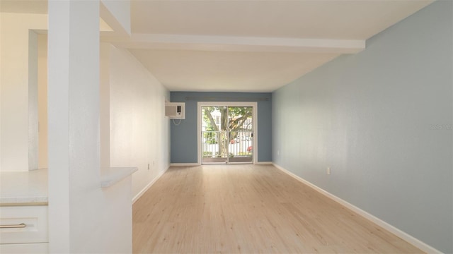 empty room featuring light wood-type flooring, a wall mounted air conditioner, and beam ceiling