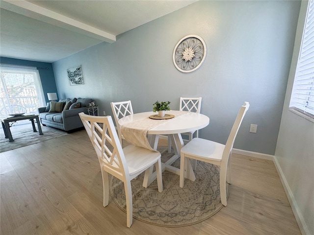 dining room featuring light wood-type flooring, beam ceiling, and baseboards