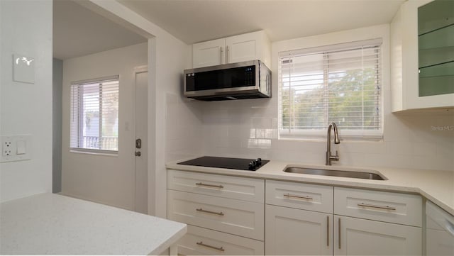 kitchen featuring tasteful backsplash, stainless steel microwave, a sink, and white cabinetry