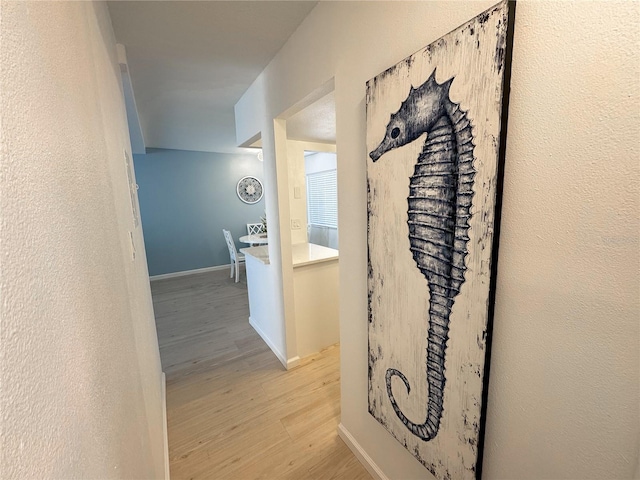 hallway with baseboards, a textured wall, and light wood finished floors