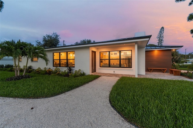 back house at dusk featuring a patio area and a lawn