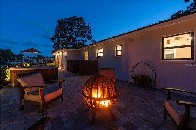 patio terrace at dusk featuring an outdoor fire pit and a hot tub