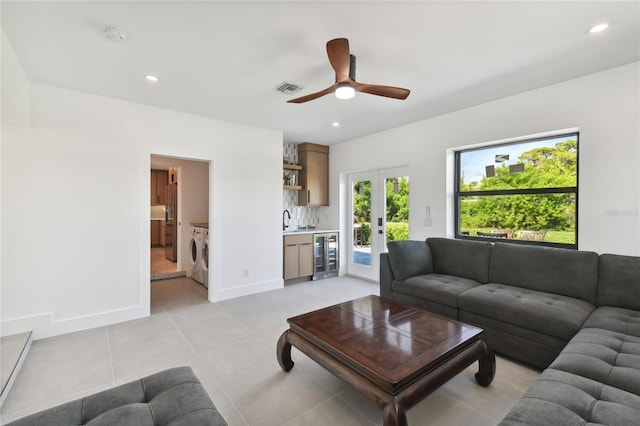 tiled living room featuring wine cooler, french doors, wet bar, ceiling fan, and washer and clothes dryer