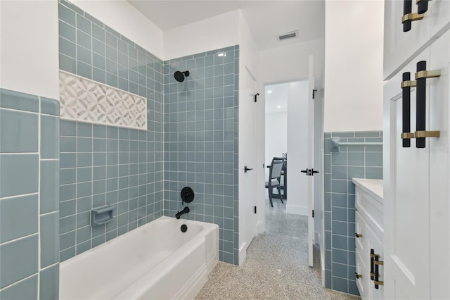 bathroom with tile walls, vanity, and tiled shower / bath