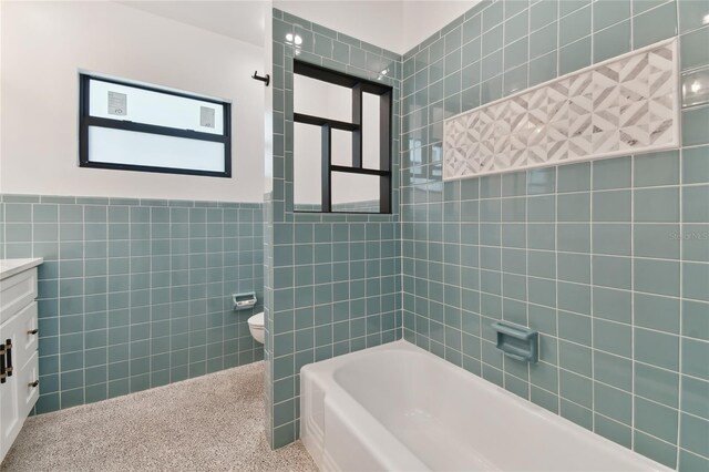 full bathroom featuring vanity, tiled shower / bath, tile walls, and toilet