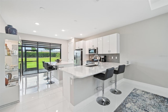 kitchen featuring a kitchen bar, kitchen peninsula, sink, white cabinetry, and stainless steel appliances