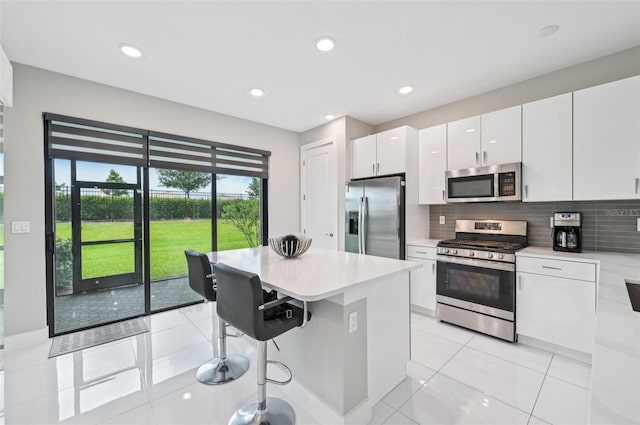 kitchen featuring light tile patterned floors, appliances with stainless steel finishes, tasteful backsplash, a kitchen breakfast bar, and white cabinets