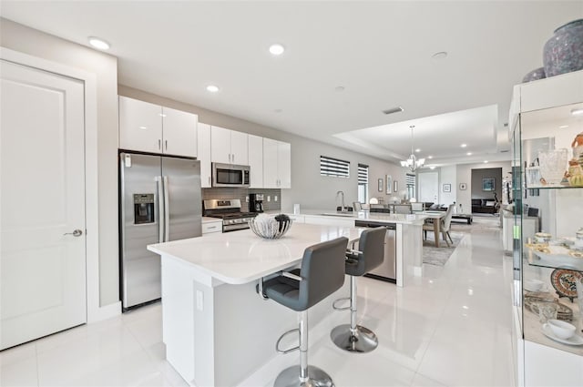 kitchen with stainless steel appliances, a notable chandelier, hanging light fixtures, white cabinets, and a breakfast bar