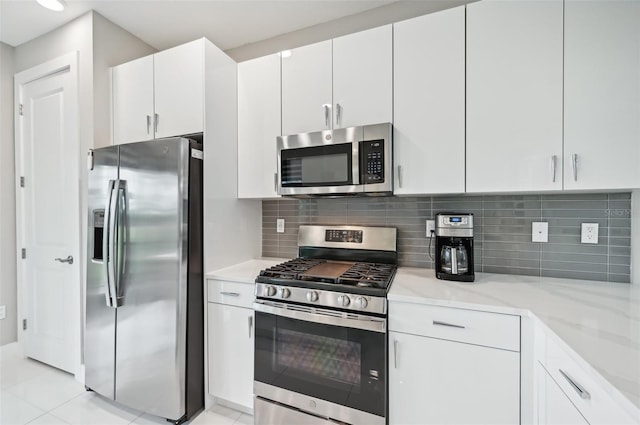 kitchen with stainless steel appliances, decorative backsplash, white cabinets, and light stone countertops