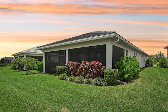 property exterior at dusk featuring a sunroom and a lawn