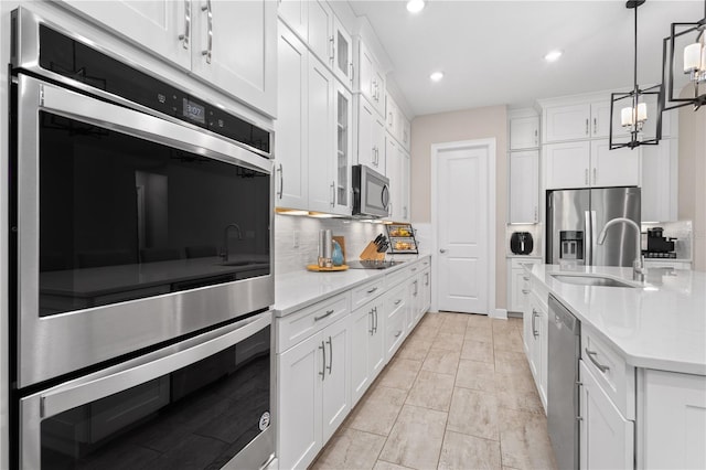 kitchen with sink, appliances with stainless steel finishes, white cabinetry, decorative backsplash, and decorative light fixtures