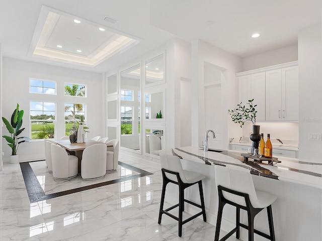 kitchen featuring white cabinets, a kitchen bar, a raised ceiling, and sink