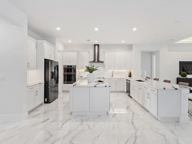 kitchen with fridge with ice dispenser, wall chimney exhaust hood, a kitchen island, double oven, and white cabinets