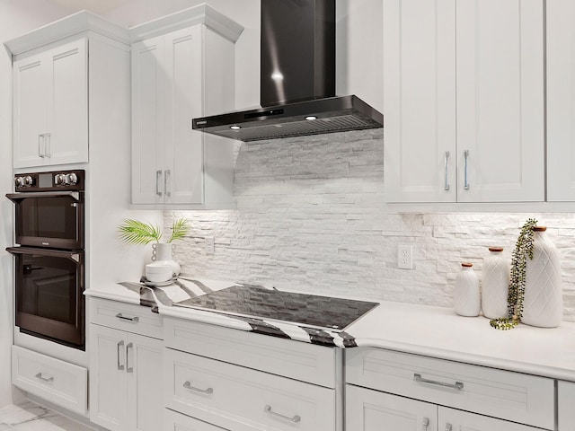 kitchen with decorative backsplash, white cabinetry, double oven, and wall chimney exhaust hood