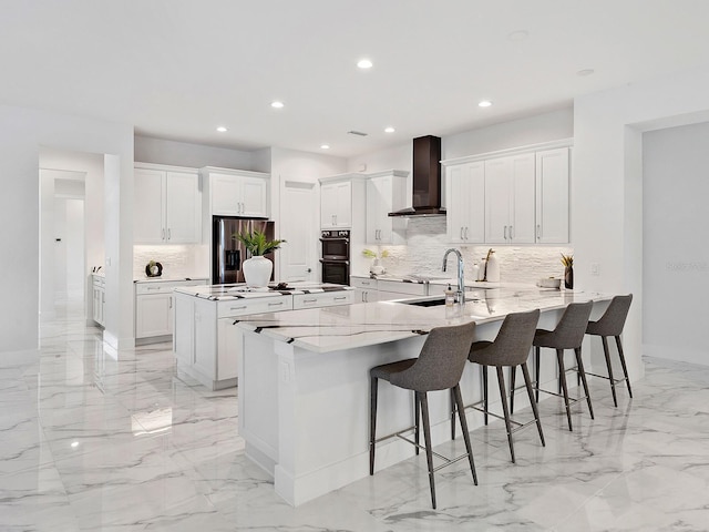 kitchen with appliances with stainless steel finishes, a spacious island, wall chimney range hood, white cabinets, and a breakfast bar area