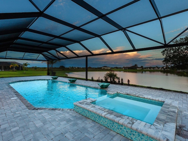 pool at dusk with an in ground hot tub, a patio, a water view, and glass enclosure