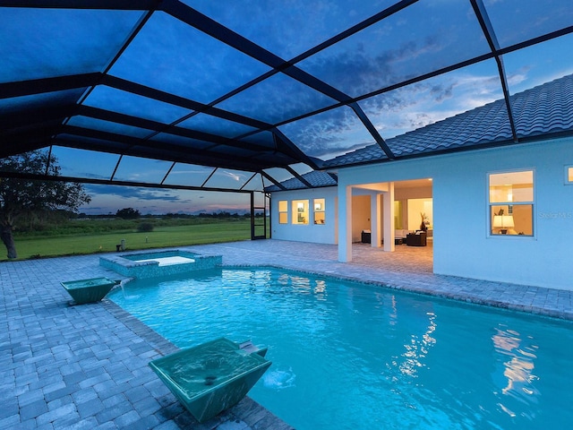 pool at dusk featuring glass enclosure, an in ground hot tub, and a patio