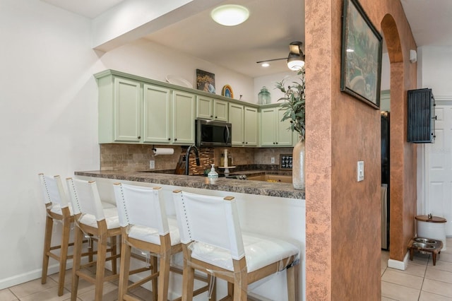 kitchen with a kitchen bar, tasteful backsplash, green cabinetry, and light tile patterned floors