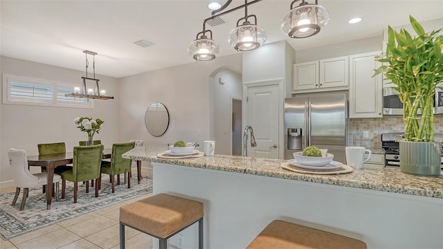 kitchen featuring hanging light fixtures, stainless steel appliances, light stone counters, decorative backsplash, and white cabinets