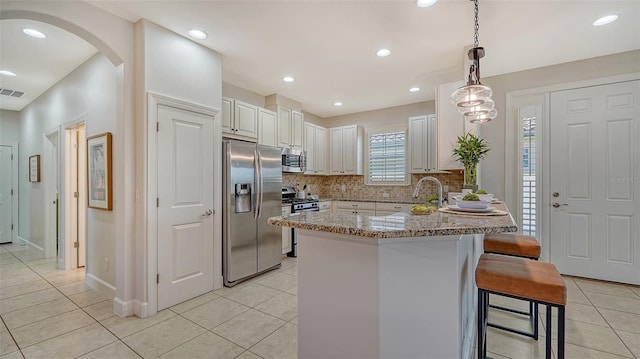 kitchen featuring appliances with stainless steel finishes, a kitchen breakfast bar, light stone counters, white cabinets, and hanging light fixtures