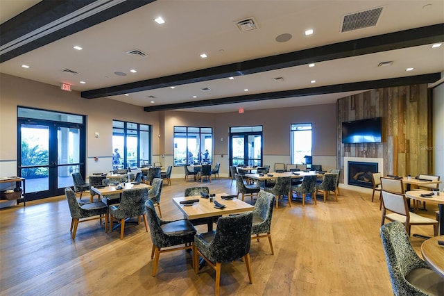 dining area with beamed ceiling, french doors, a large fireplace, and light hardwood / wood-style floors