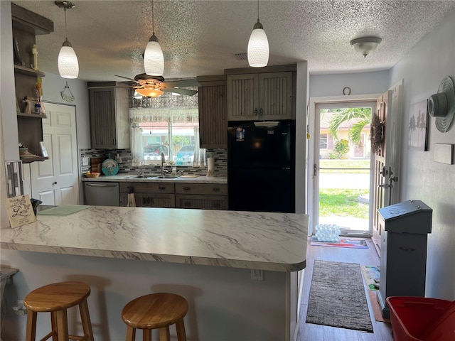 kitchen with black fridge, stainless steel dishwasher, kitchen peninsula, a kitchen bar, and sink