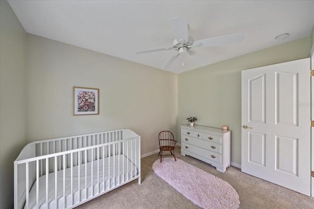 carpeted bedroom featuring a crib and ceiling fan