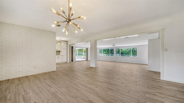 unfurnished living room featuring light hardwood / wood-style floors, a notable chandelier, and brick wall