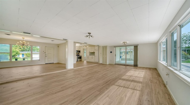 unfurnished living room with a healthy amount of sunlight, a notable chandelier, and light hardwood / wood-style flooring