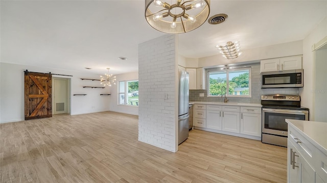 kitchen with white cabinetry, backsplash, a barn door, light hardwood / wood-style floors, and appliances with stainless steel finishes