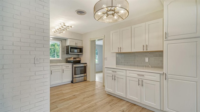 kitchen with appliances with stainless steel finishes, white cabinets, an inviting chandelier, backsplash, and light hardwood / wood-style floors