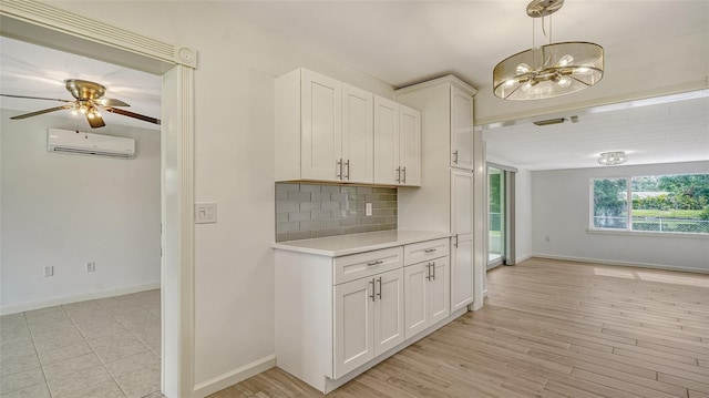 kitchen with tasteful backsplash, ceiling fan with notable chandelier, white cabinets, light wood-type flooring, and a wall mounted AC