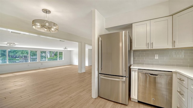 kitchen featuring light hardwood / wood-style floors, appliances with stainless steel finishes, hanging light fixtures, and backsplash