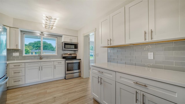 kitchen with white cabinets, stainless steel appliances, tasteful backsplash, and light wood-type flooring